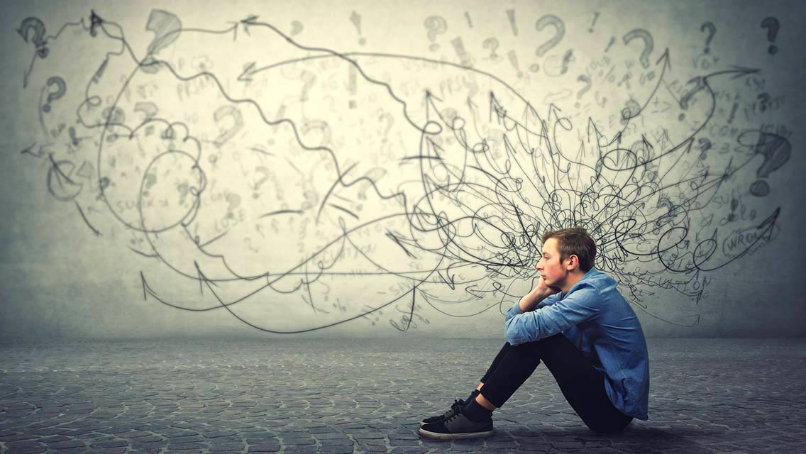 Upset and tired teenager sitting on the floor keeps hand to cheek looking thoughtfully and hopeless with an illustration of chaos emanating from his head.