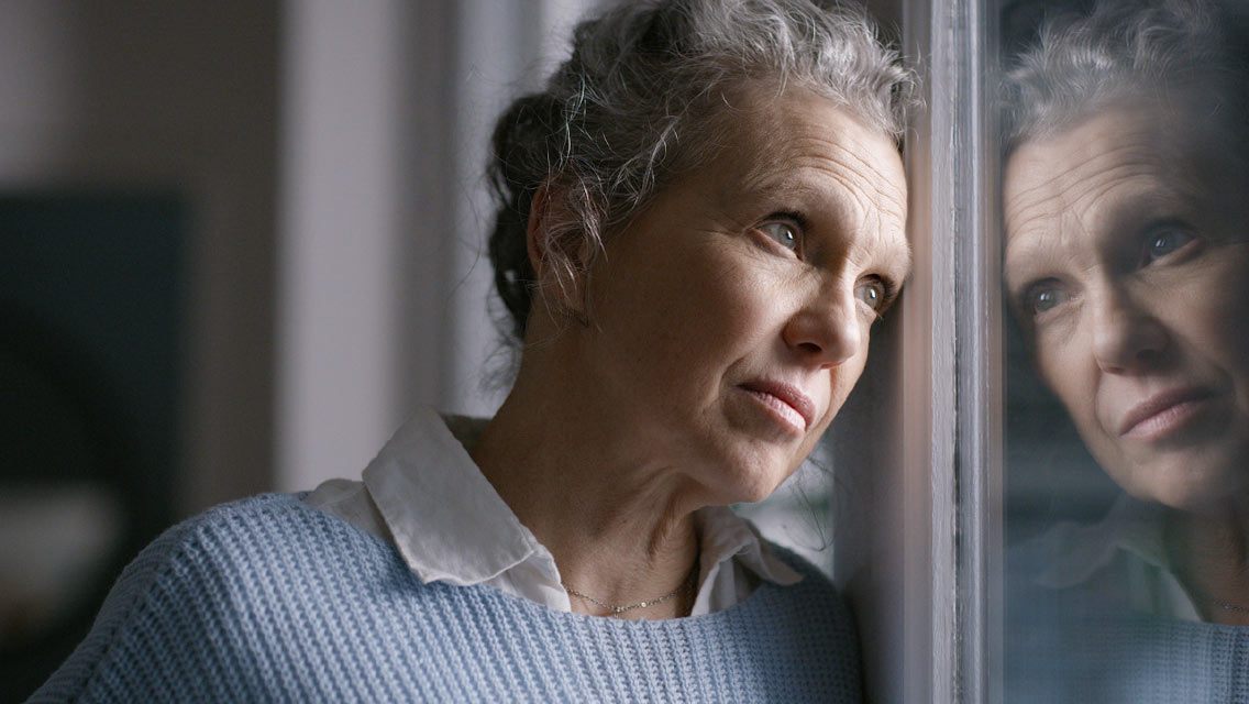 a senior woman gazes forlornly out the window