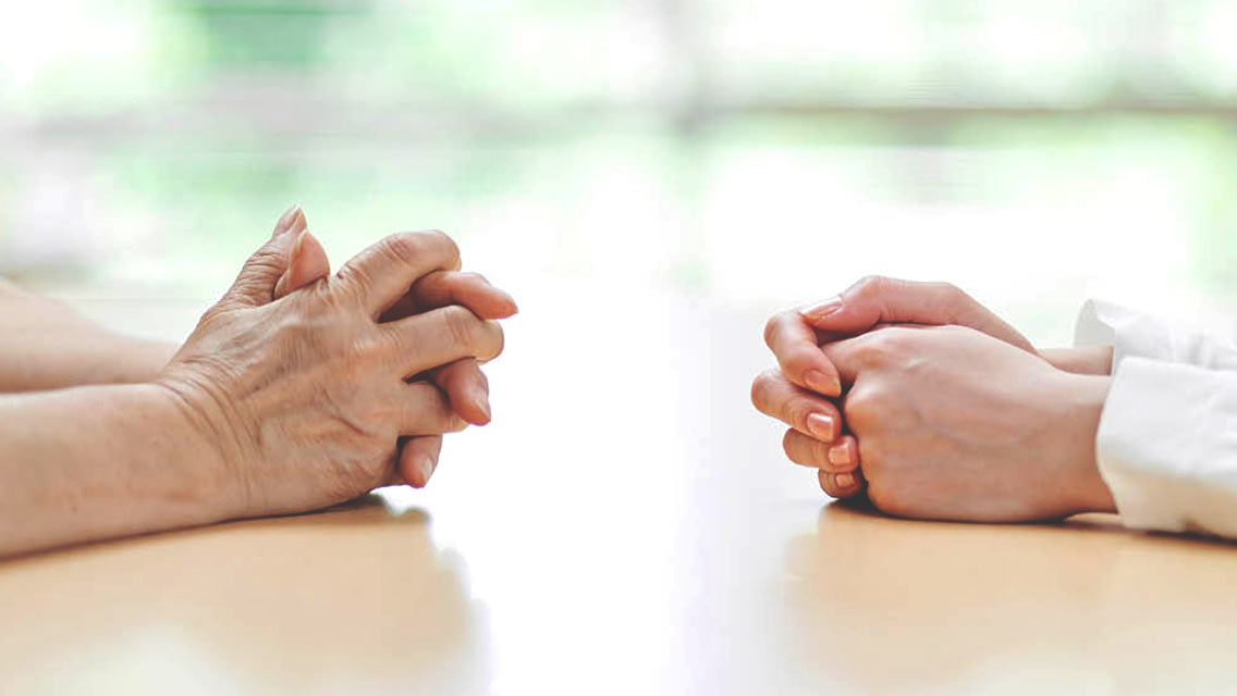 folded elderly hands sit across a table from younger folder hands