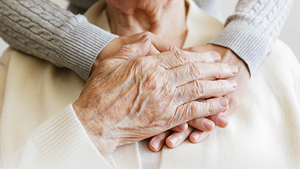 a woman holds her hands over an elderly person's heart