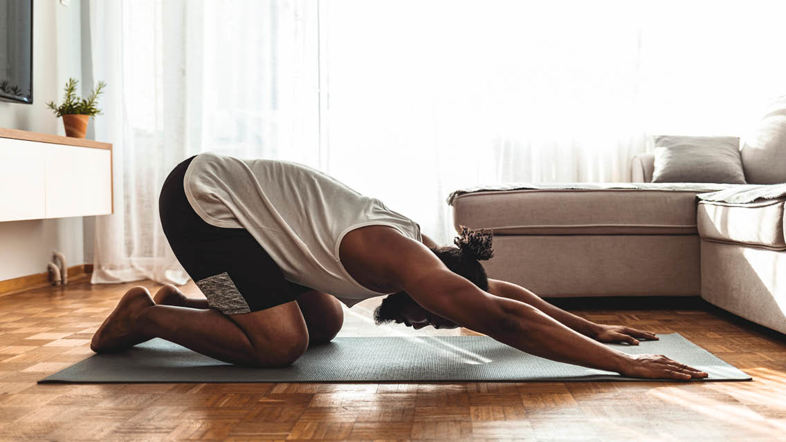a man holds extended child's pose in his living room