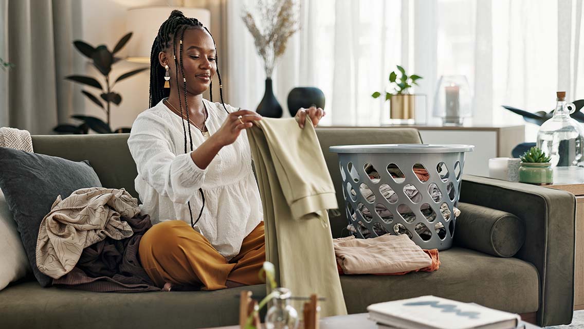 a woman folding washing on a sofa in the living room of her home to tidy