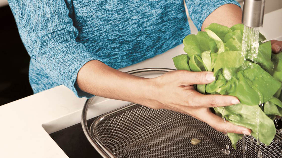 Woman washing greens in a kitchen sink.