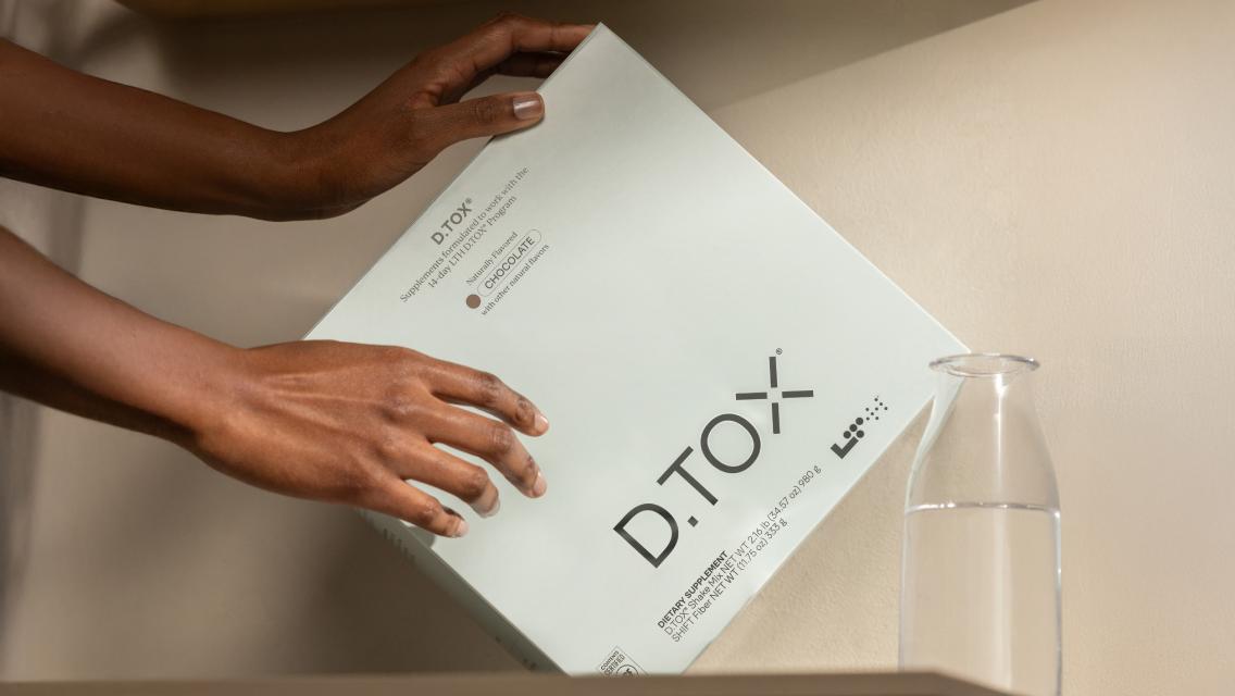 A woman's hands setting the D.TOX kit on a counter next to a glass of water.