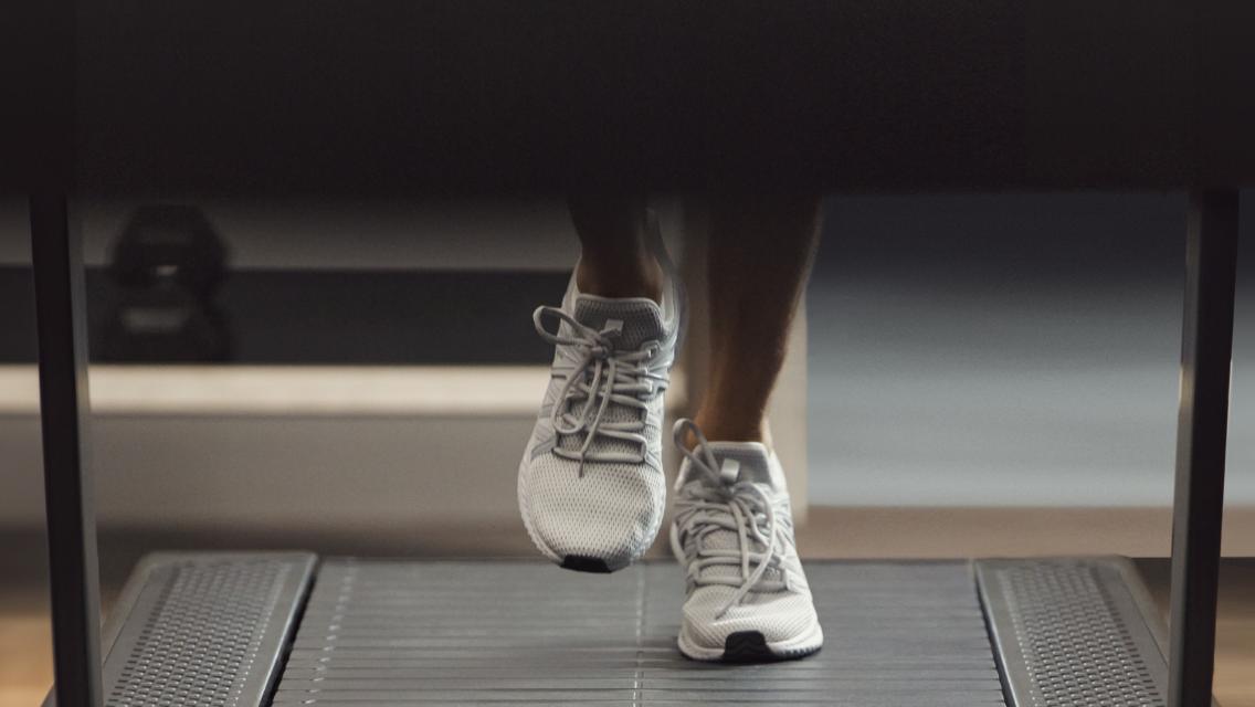 Close-up of two feet with white sneakers walking on a treadmill.