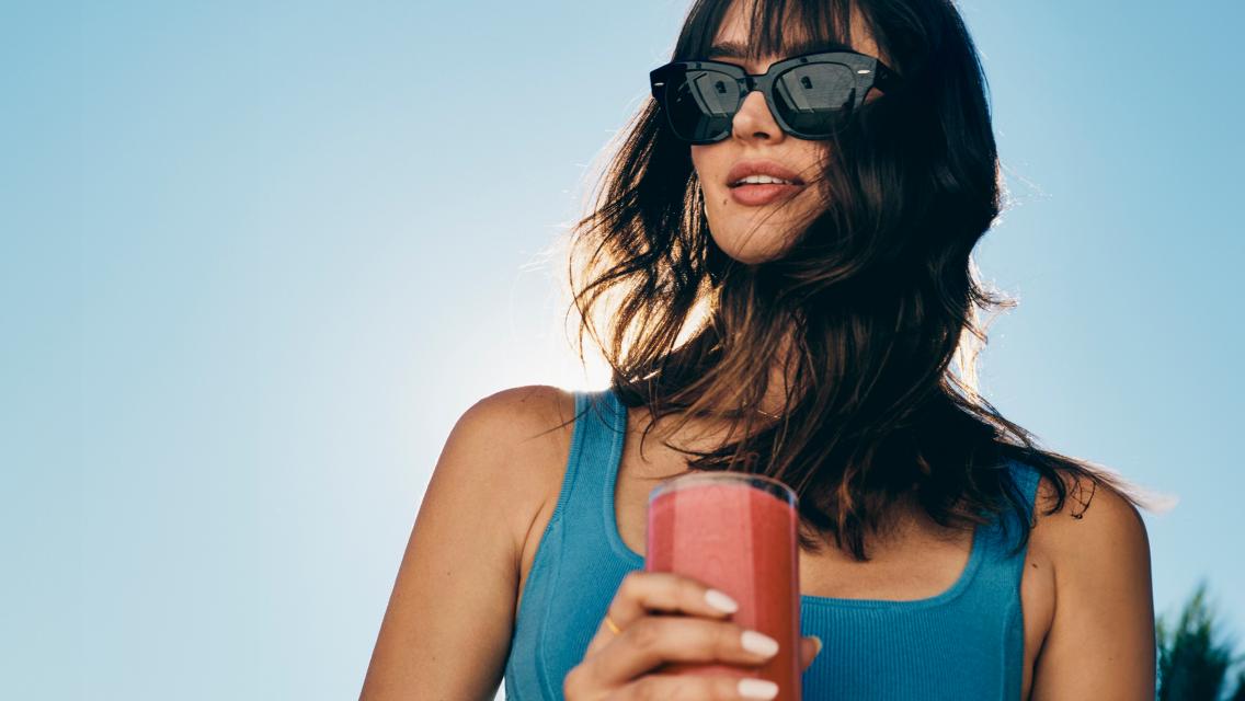 A woman holding a berry-colored shake while outdoors on a sunny day.