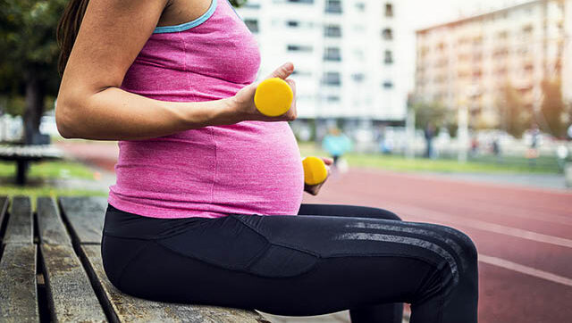 Pregnant woman sitting on bench lifting weights