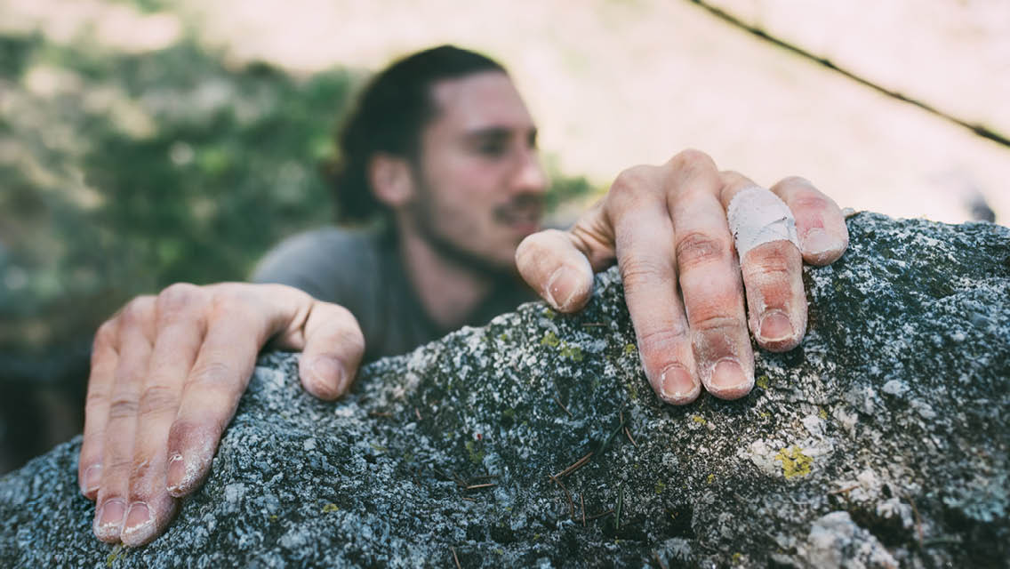 hands holding onto the top of a boulder