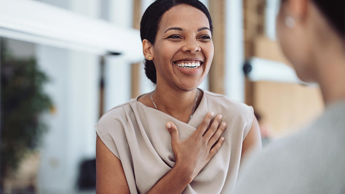 a woman smiles while she places her hand over her heart.