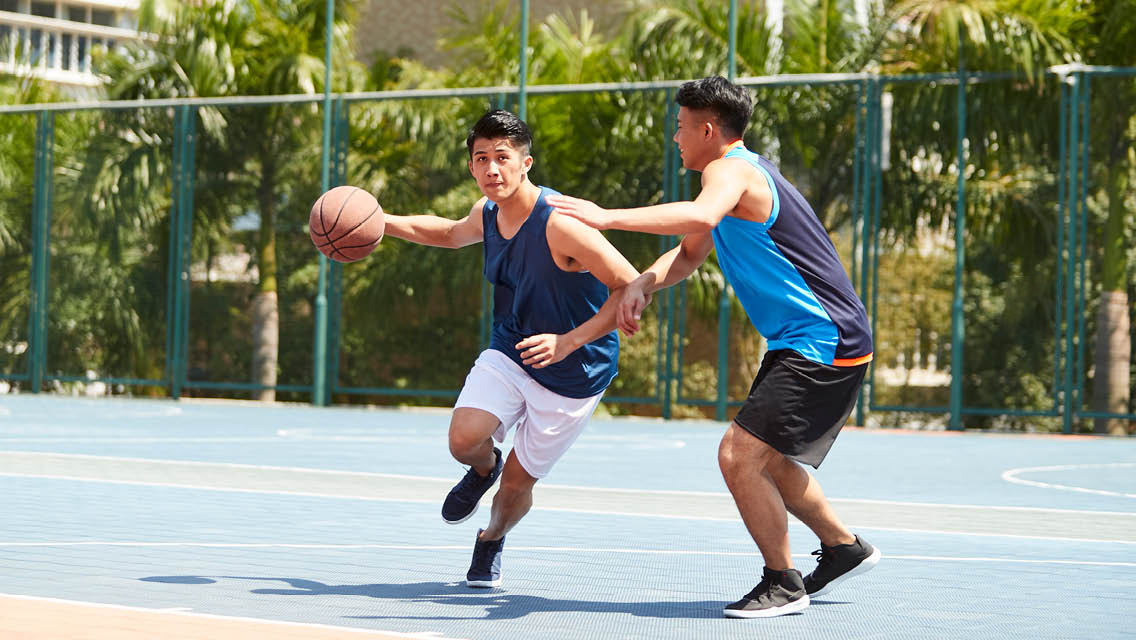 two guys play basketball on an outside court