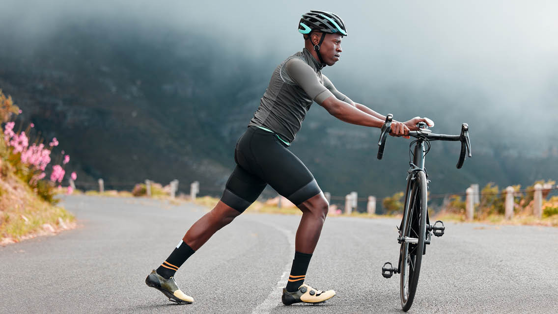 a man stretches his calf while holding his bike