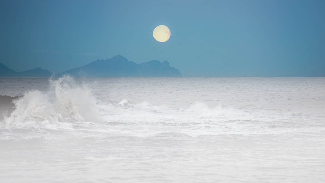 a moon scape over an ocean with crashing waves