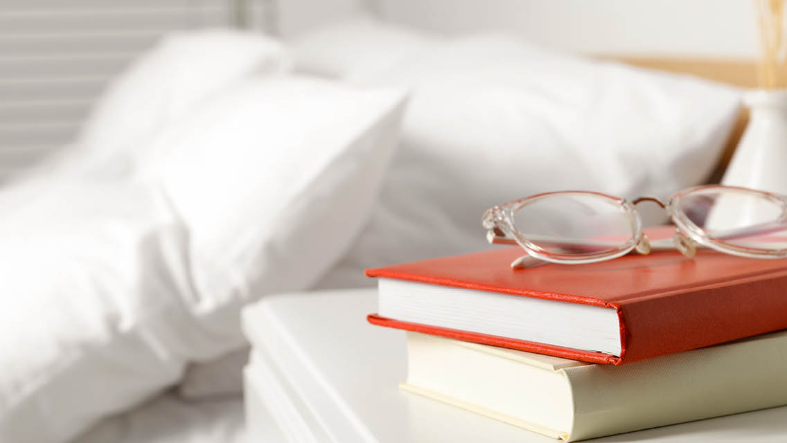 books and reading glasses rest on a nightstand