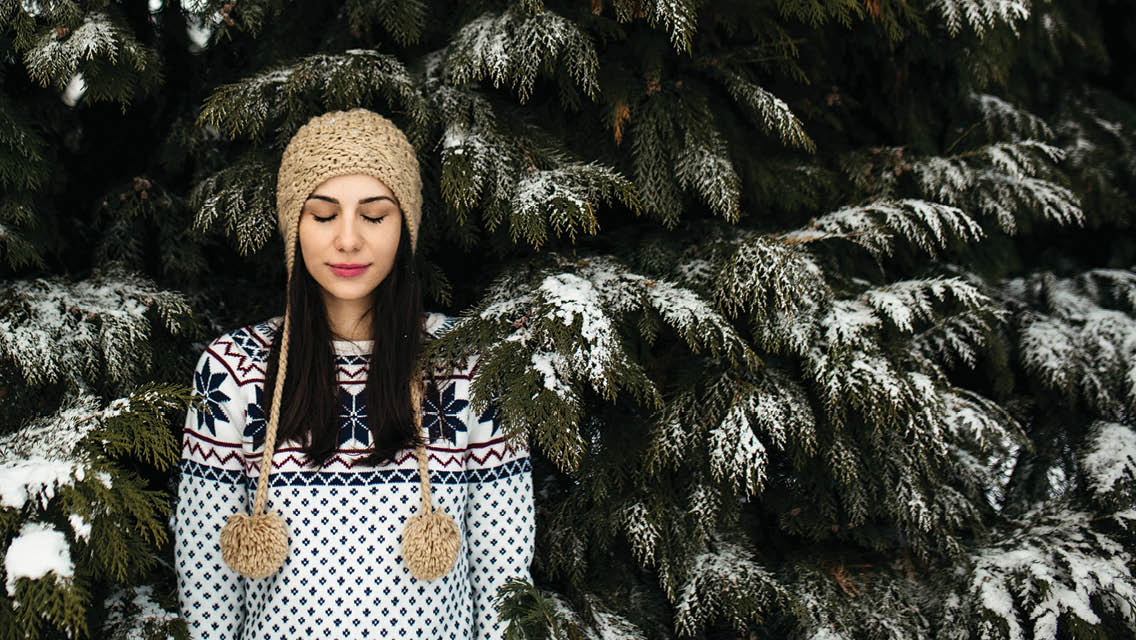 a woman stands in front of a snowy pine tree with her eyes closed