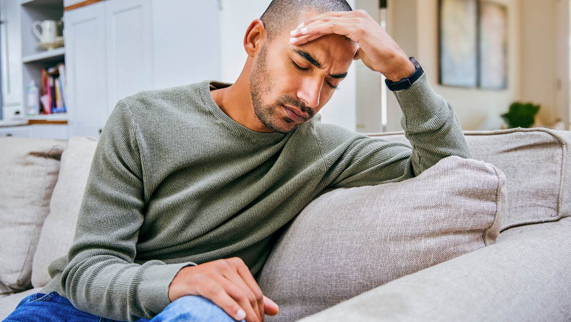 a man sits on a couch holding his head