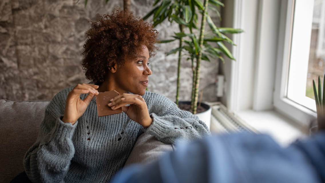 a woman eats chocolate while looking our the window.