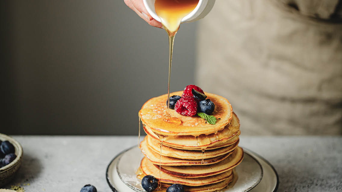 a person pours syrup on pancakes