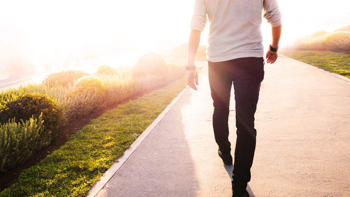 a man walks down a sidewalk at sunrise