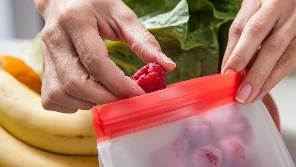 a person fills a colorful zip top baggie with fresh fruit
