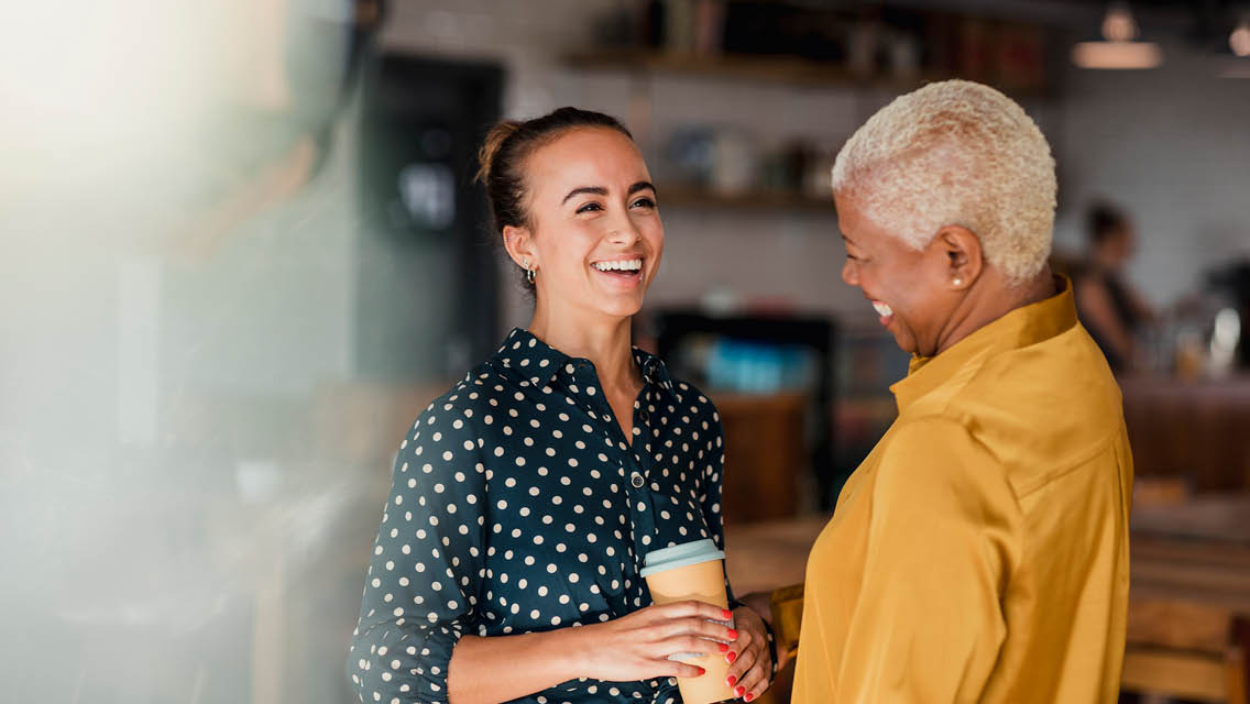 two women talk and laugh at a coffee shop