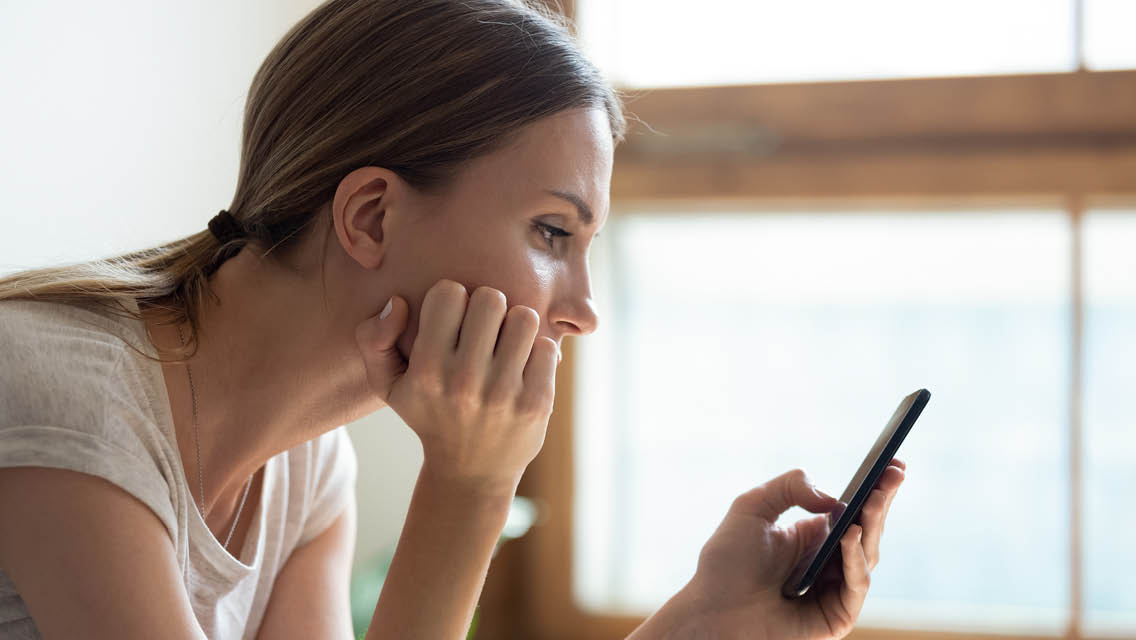 a woman looks begrudgingly at her cell phone