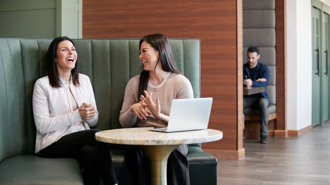 two women sitting at desk smiling together