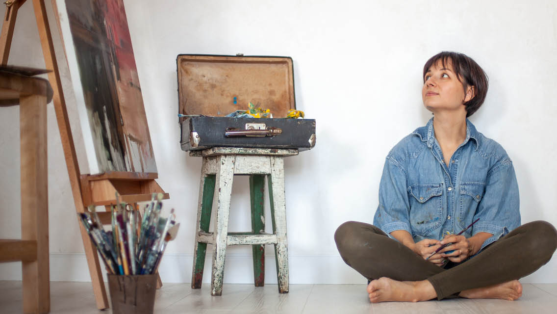 a woman sits on the ground looking at her painting