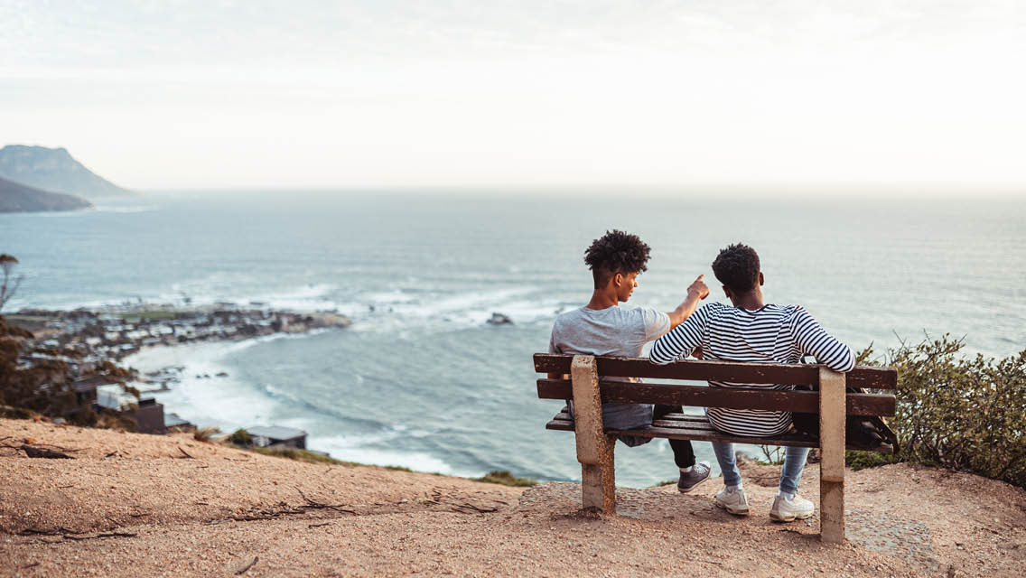 two people sit on a bench overlooking the ocean