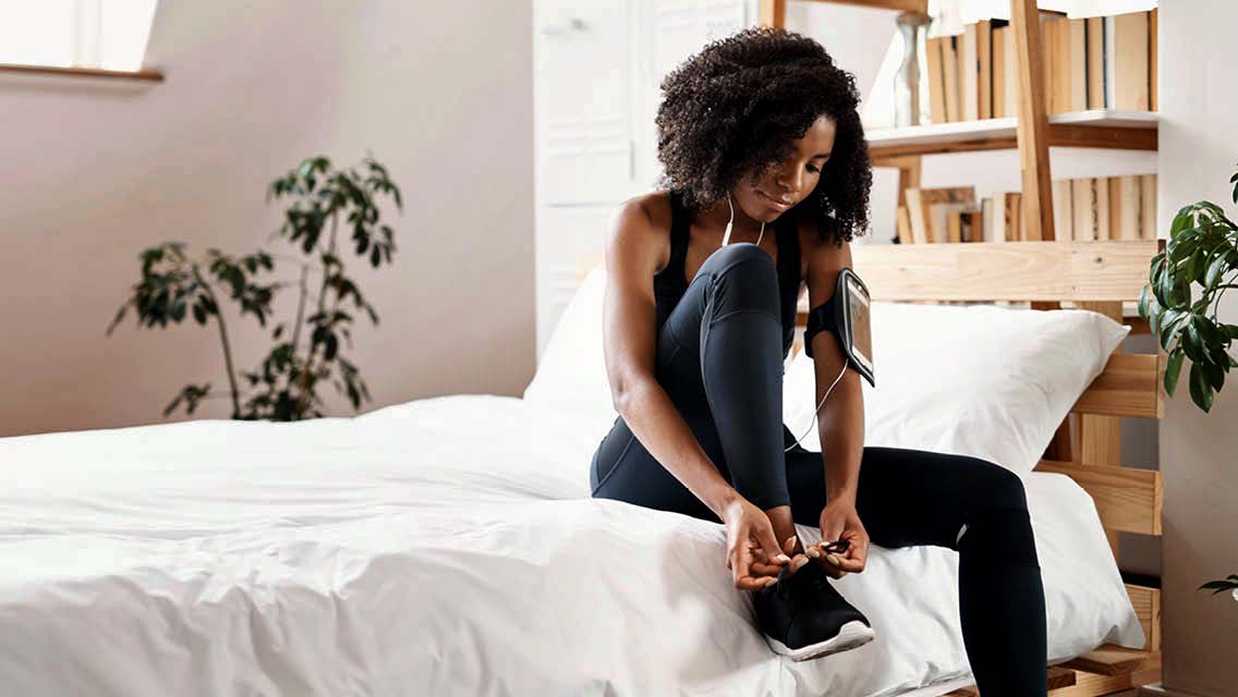 a person puts tennis shoes on while sitting on her bed.