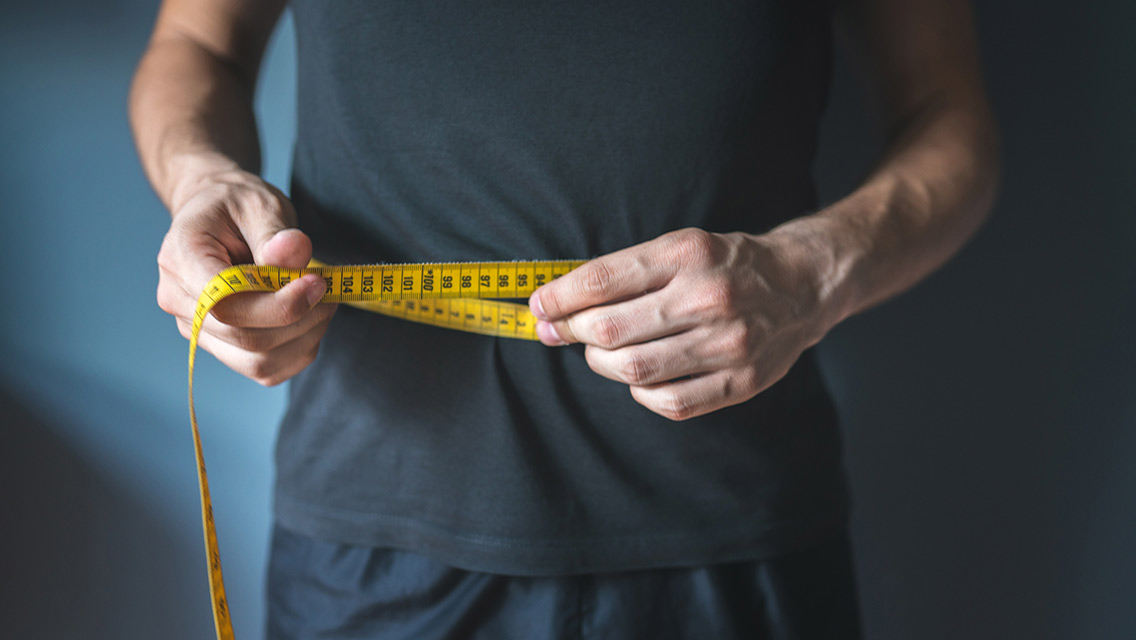 A person measures their waist with a measuring tape.