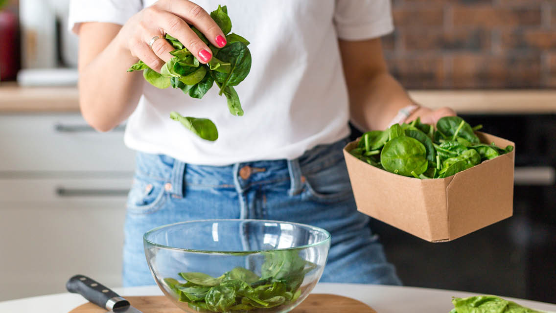 a person filling a bowl with spinach