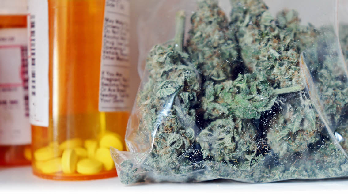 a baggie of marijuana sits next to a bottle of prescriptions meds