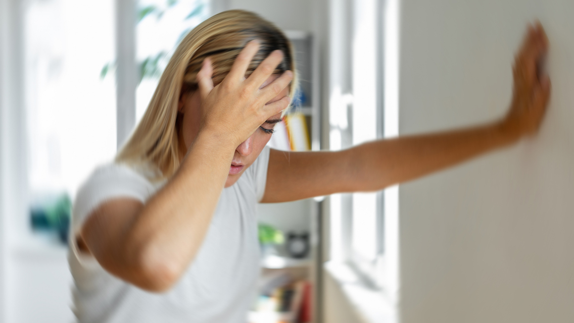 a woman places her hand on a wall during a dizzy spell