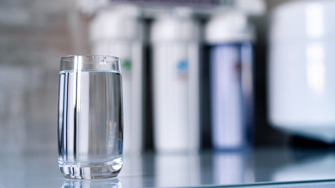 a glass of water on a counter with drinking bottles behind it