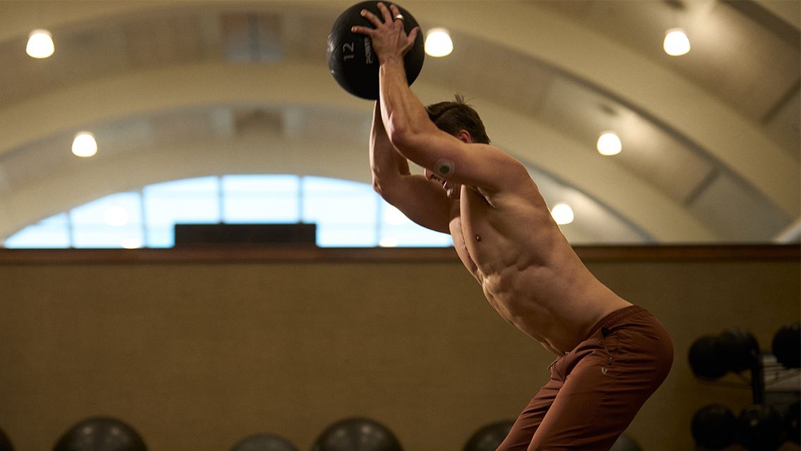 a man wearing a glucose monitor prepares to do a med ball slam