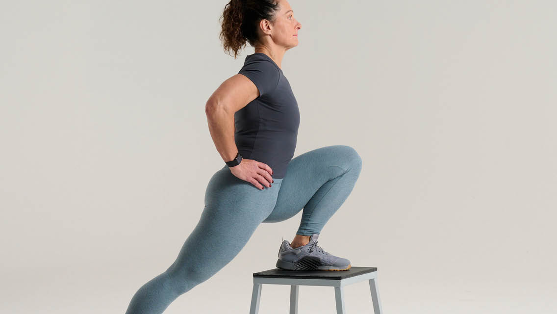 a woman holds a lunge position with one leg on a stool