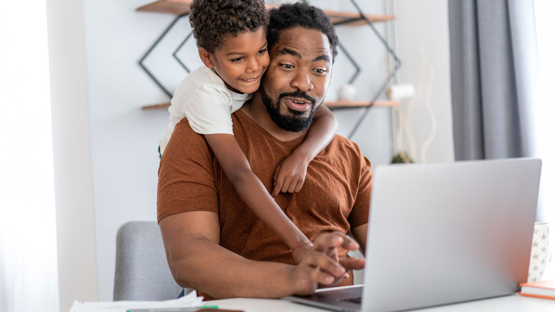 a man works while his son hangs over his shoulder